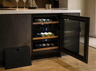 Compact electric multi-zone wine cellar under a modern kitchen counter, open to show organized bottles in different temperature zones, with digital controls and soft interior lighting.