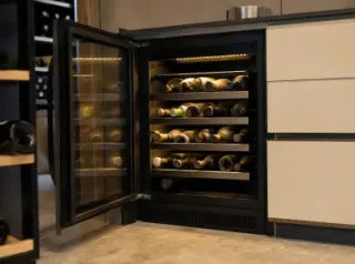 Compact electric wine cellar under modern kitchen counter with glass door, touchscreen controls, and neatly stored bottles