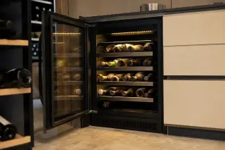 Compact electric wine cellar under modern kitchen counter with glass door, touchscreen controls, and neatly stored bottles