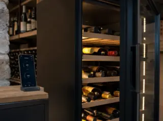 Modern connected wine cellar cabinet in a contemporary home, smartphone app showing controls next to neat wine bottle racks.
