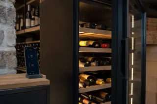 Modern connected wine cellar cabinet in a contemporary home, smartphone app showing controls next to neat wine bottle racks.