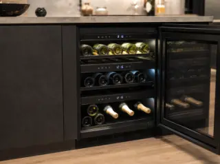 Compact electric multi-temperature wine cellar built into a modern kitchen, door open to show organized wine bottles in different temperature zones with digital controls and LED lighting.