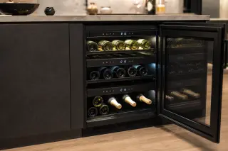 Compact electric multi-temperature wine cellar built into a modern kitchen, door open to show organized wine bottles in different temperature zones with digital controls and LED lighting.