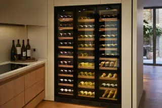 Built-in multi-zone wine cellar in a modern kitchen, glass front showing three zones with organized wine bottles and digital controls.